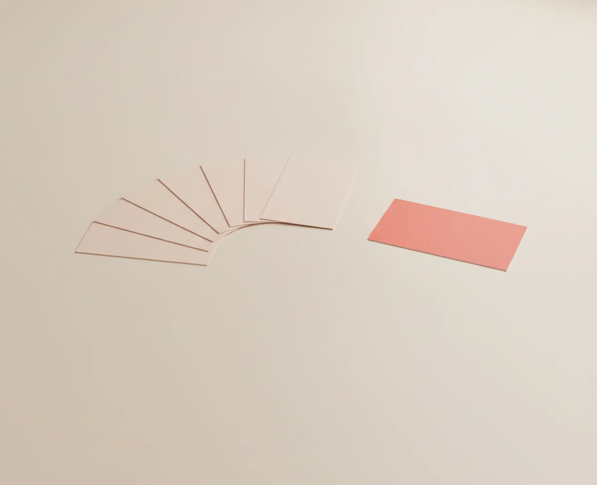 Six blank blush cards fanned into a wide arc on a warm off-white floor, with one coral card lifted out of the fan and set down apart from the others