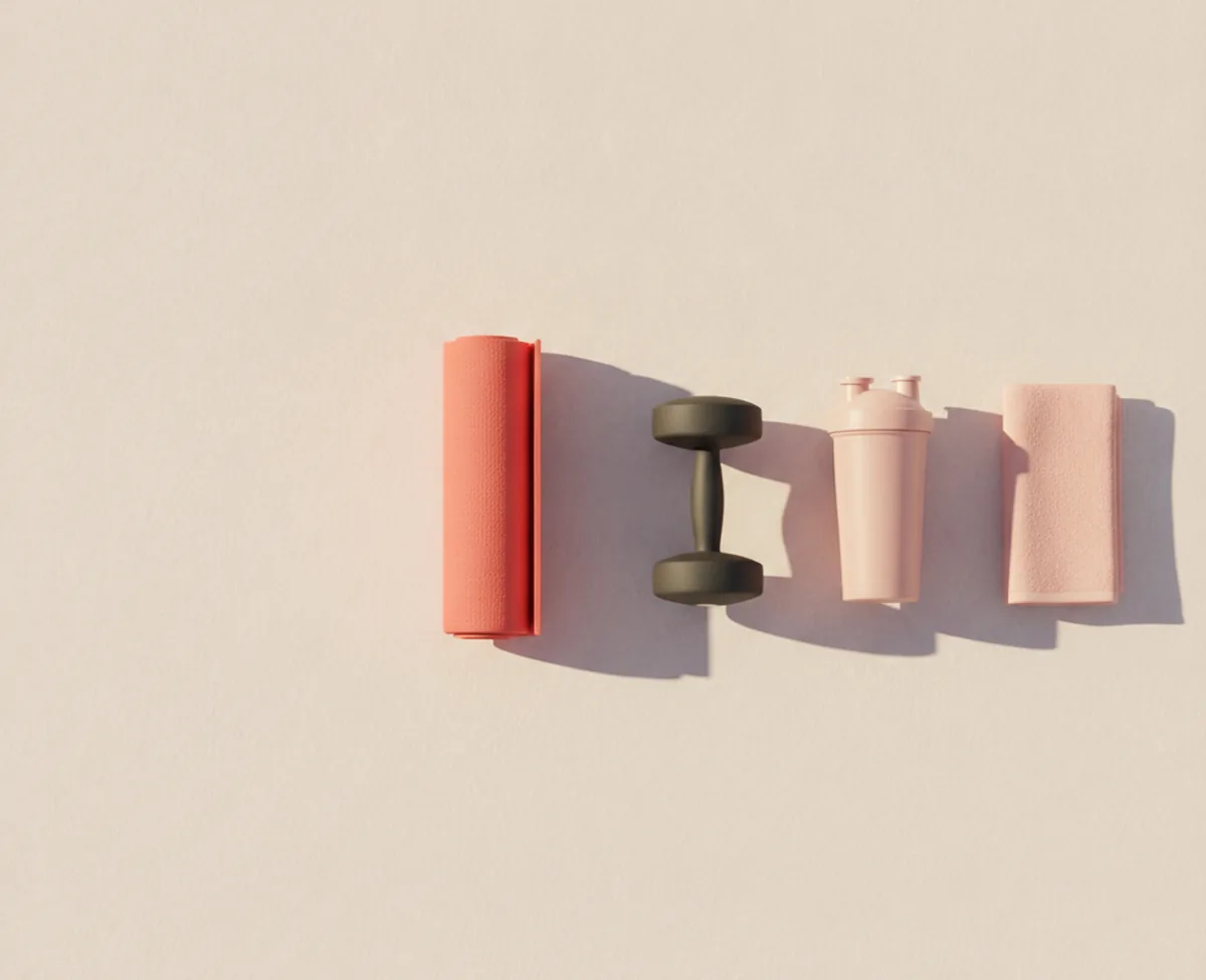 An overhead view of a pale floor with a rolled coral exercise mat, a small matte dumbbell, a plain unmarked shaker bottle and a folded blush towel laid out in a row