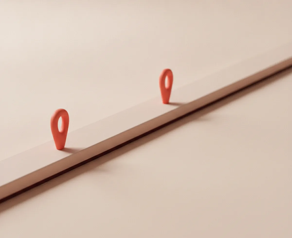 Two coral pin markers standing on a long pale rail that crosses a warm off-white floor, one near the start and one much further along, with empty rail between them
