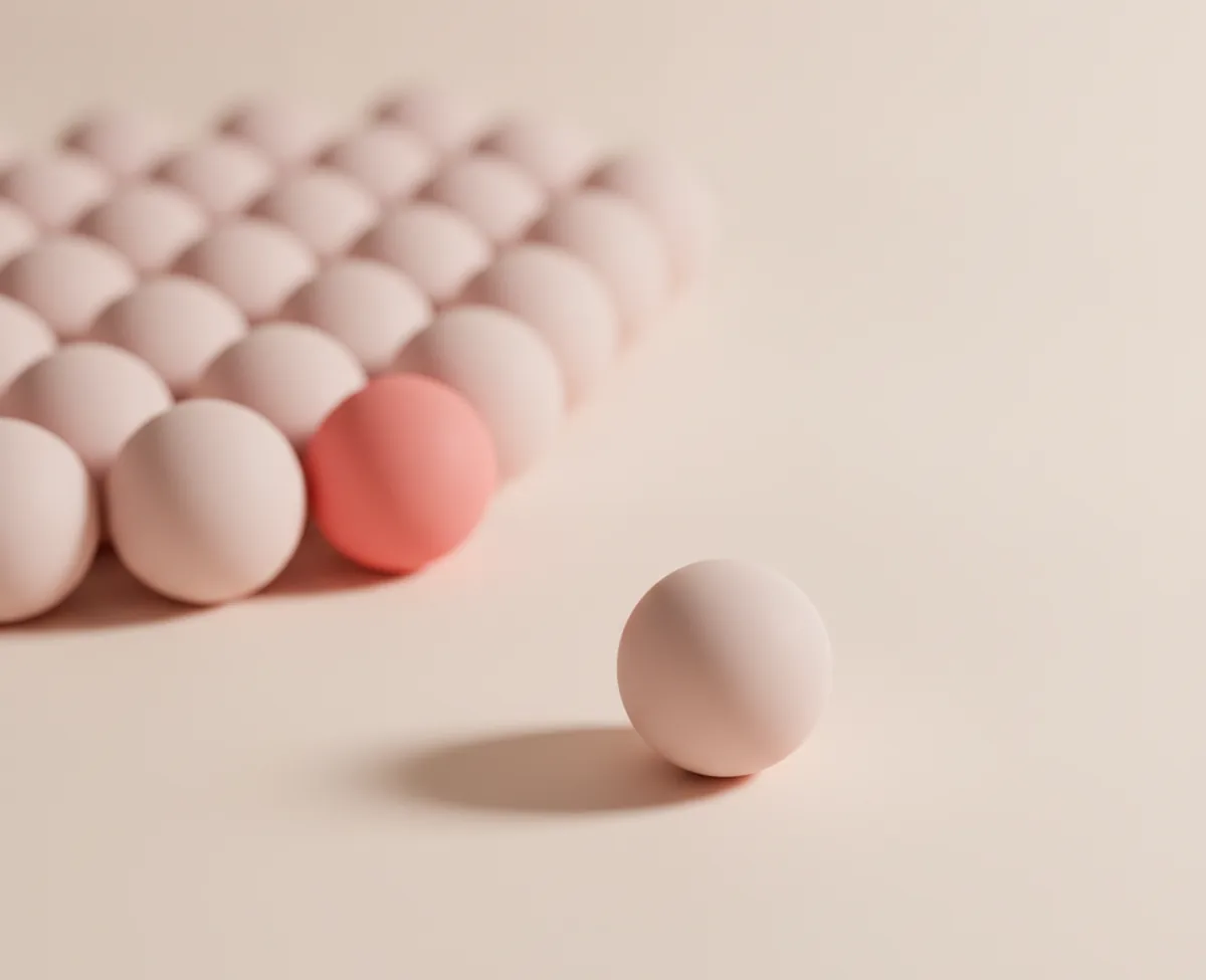A single matte blush sphere resting alone on a warm off-white floor, with a large close-packed field of identical spheres behind it and one coral sphere at its near edge