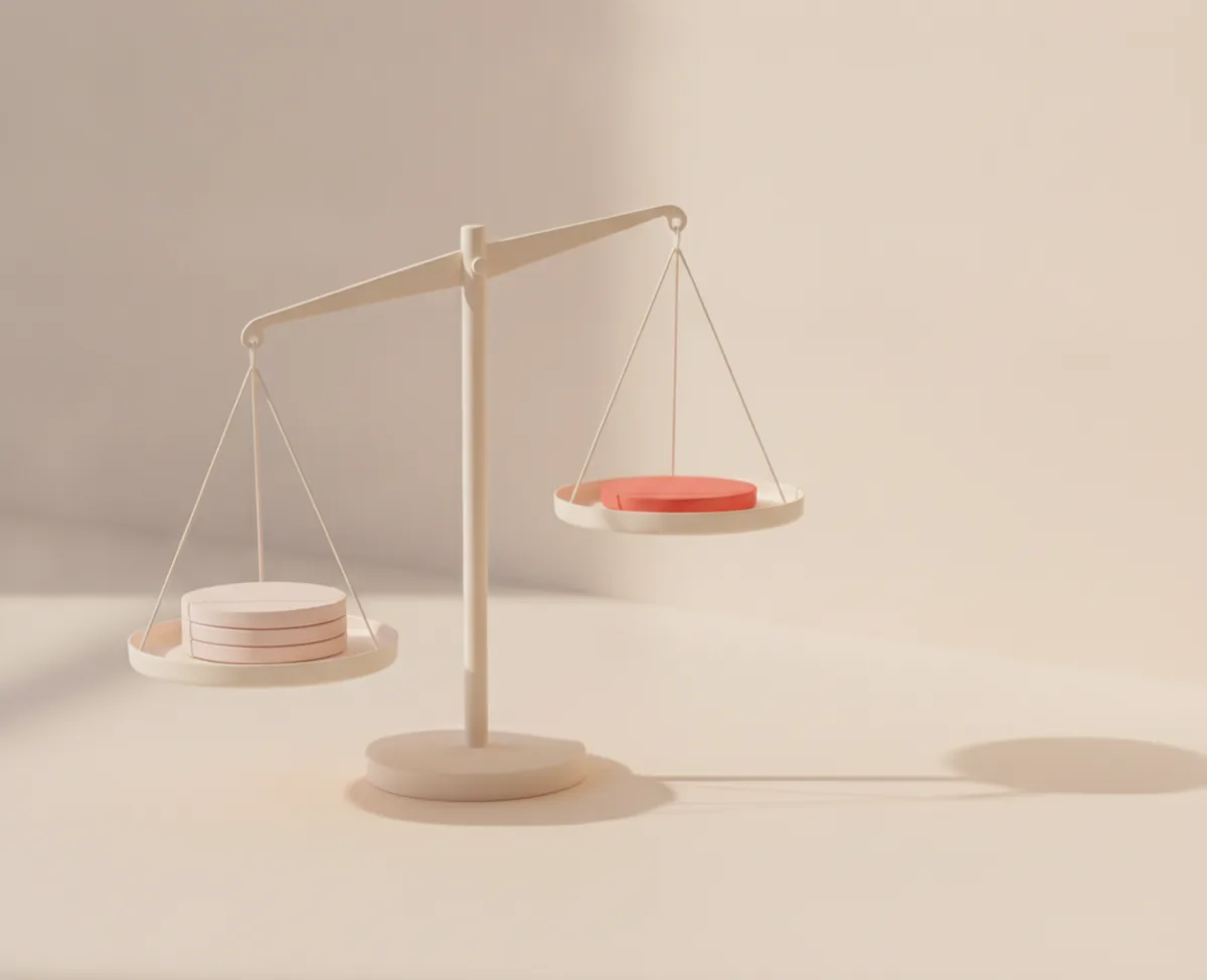 A matte balance scale on a warm off-white surface: the lower pan holds a short stack of blank blush discs, the raised pan carries a single coral disc