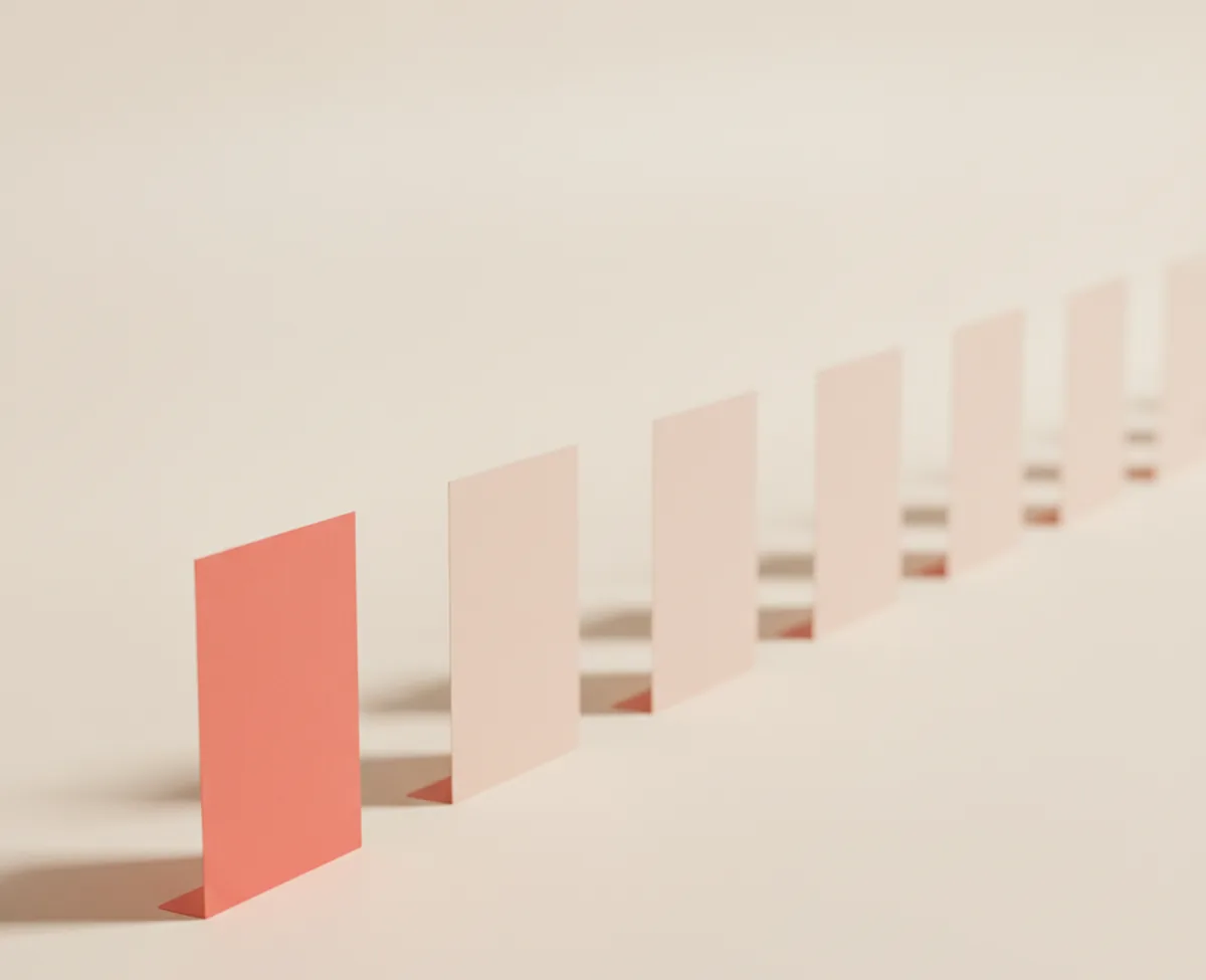 A coral card standing at the head of a long line of blank blush cards receding across a warm off-white surface, each casting its own small shadow